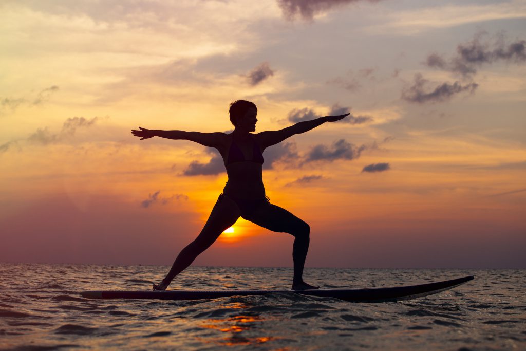 Woman practicing SUP yoga at sunset, meditating on a paddle board.